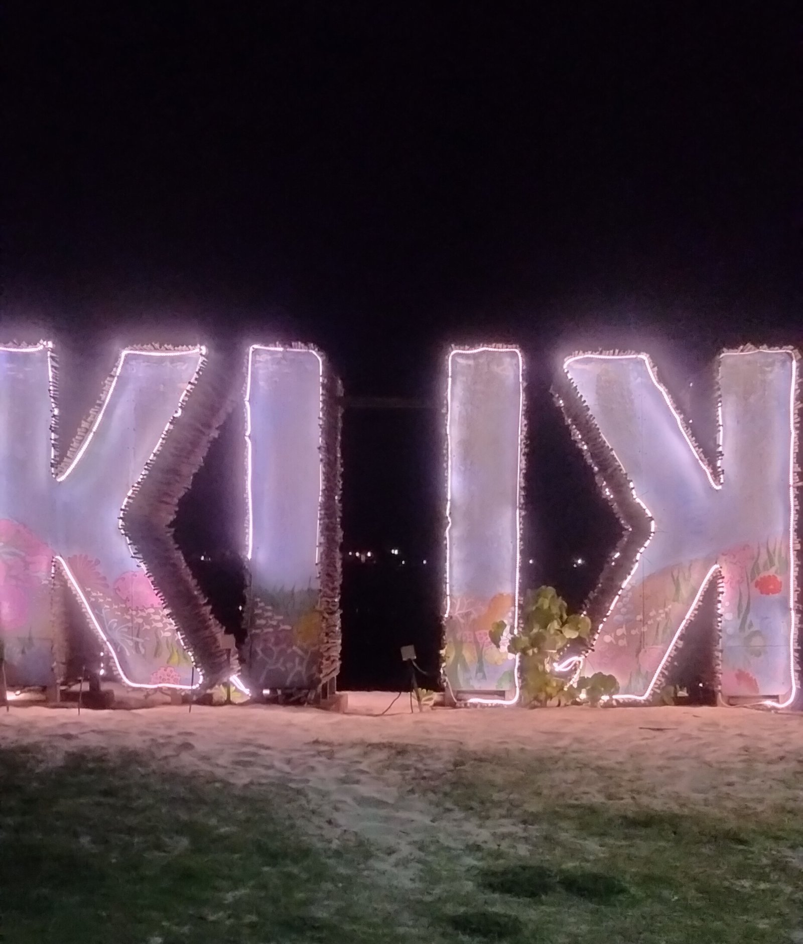 Illuminated "KIKI" letter sign prominently displayed on the beachfront at night, showcasing the iconic branding of Kiki Beach Island Resort.