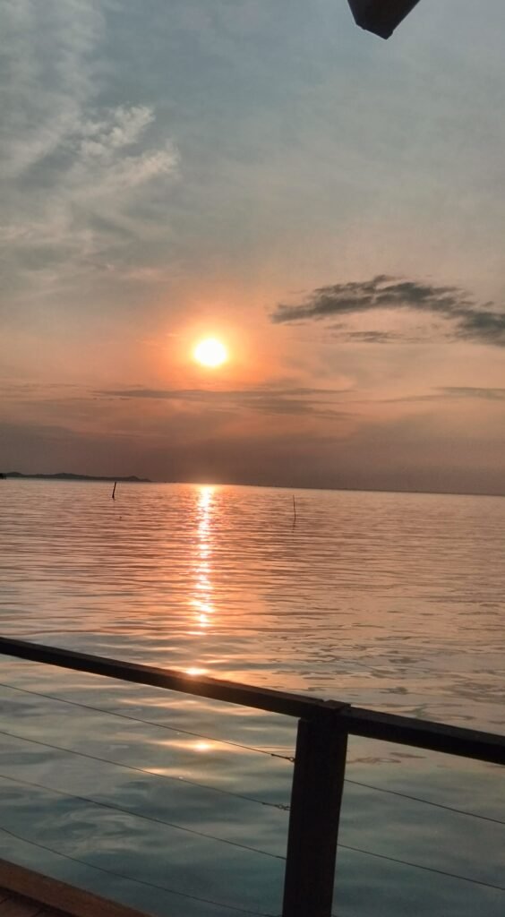 Wooden low-tide jetty leading across the water toward a mangrove area during sunset, symbolizing the local area near the batam resort with beach.