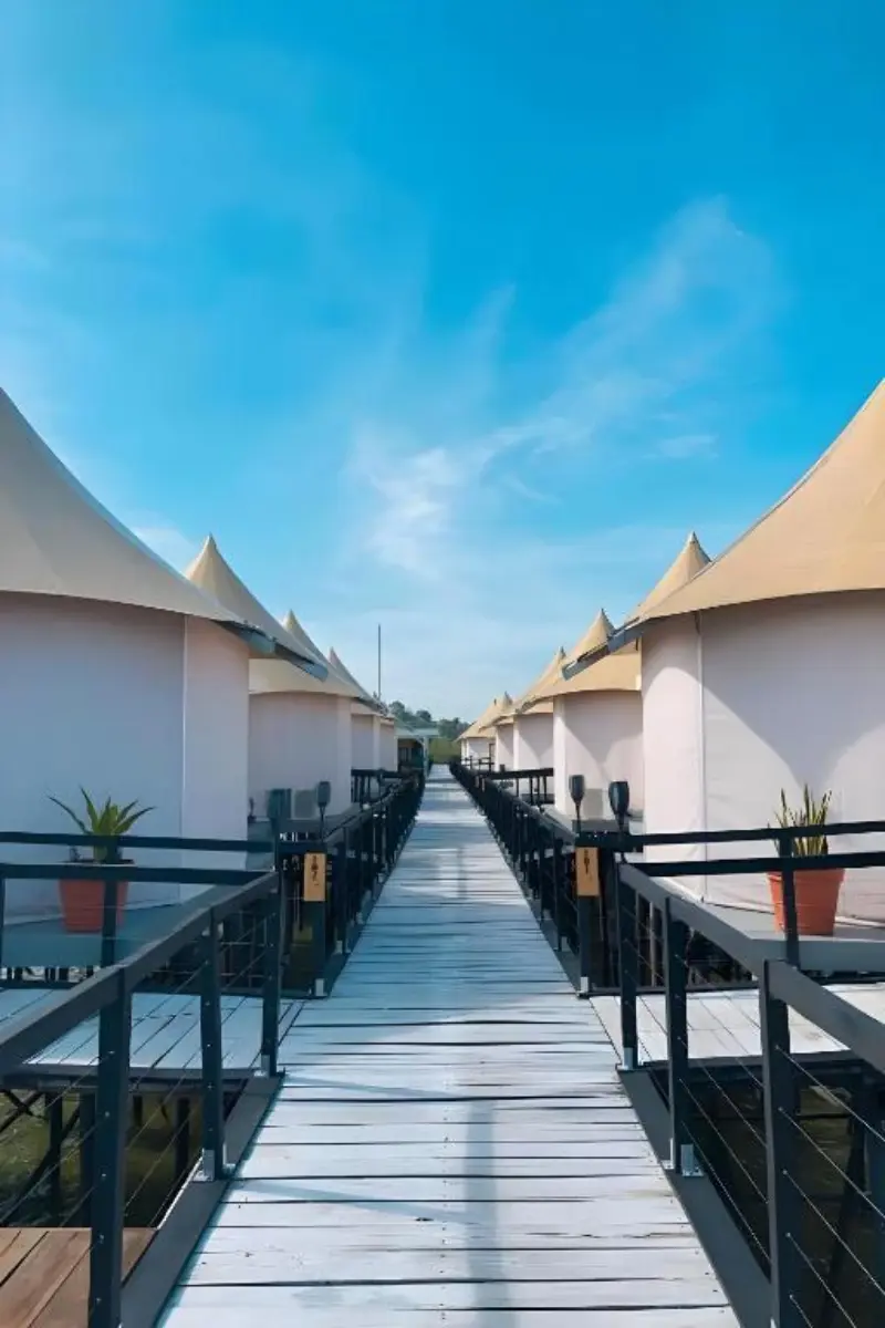 Wooden boardwalk connecting the rows of glamping tents under a clear blue sky at Kiki Beach.
