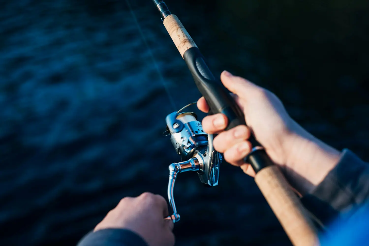 Close-up of a guest's hands reeling a fishing rod over dark water, emphasizing the hands-on fishing experience at Kiki Beach Island Resort.