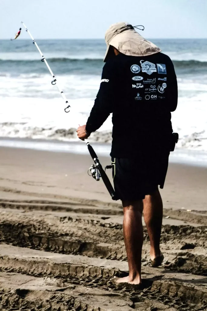 Silhouette of two guests fishing from a rocky outcrop against a bright sunset, symbolizing the fishing activity available at the batam resort with beach.