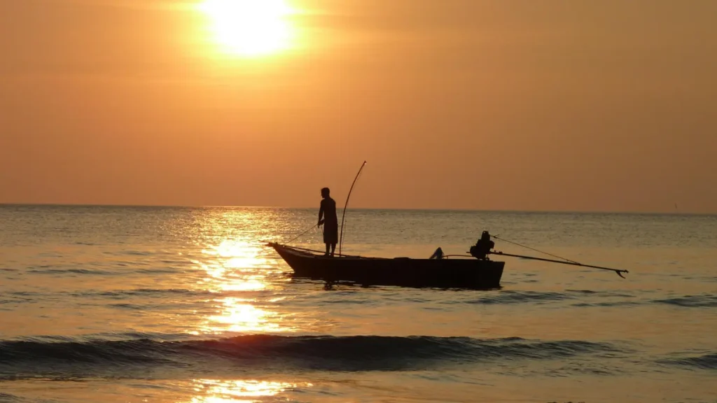 Silhouette of two guests fishing from a rocky outcrop against a bright sunset, symbolizing the angling experience at our batam resort with beach.