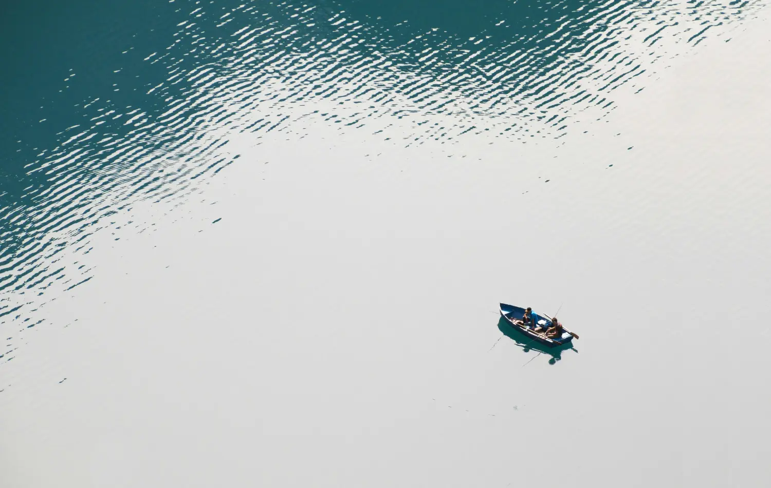 Aerial view of a small fishing boat in the middle of the open ocean, representing the Deep Sea Fishing activity at Kiki Beach Island Resort.